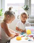 Sister and brother, sibling children molding from modeling clay together at the table. Sibling relationships and joint creativity at home in a sunny apartment.