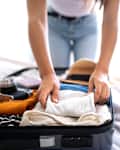 Unrecognizable young woman packing suitcase for summer vacation trip.