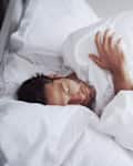 Sleeping, tired and man in bed in home for relaxing on weekend morning with dreaming in rem. Fatigue, snooze and male person with pillow and blanket for resting afternoon nap in bedroom at apartment.
