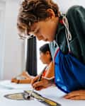 ocused boy painting with paintbrush on paper during art class at elementary school