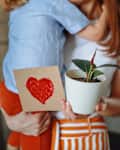 Toddler gives his mom a heart-shaped card and a potted ficus plant for Mother's Day