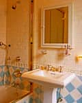 Bathroom featuring a shower with glass doors, gold fixtures, a white pedestal sink, and decorative tile accents.