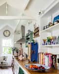 Galley style white kitchen with pitched roof, wooden worktops and open shelving. The walls are adorned with boats made by Rachel Sumner from recycled wood and found materials.