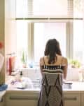 Rear view of woman at kitchen sink in front of window doing dishes