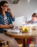 Mom working on computer at the kitchen table while toddler daughter colors