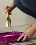 A person dipping a paintbrush into a pink paint tray