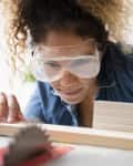 Mixed Race woman cutting wood with saw