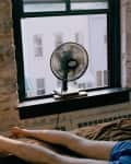 A man lying on a bed with a fan blowing