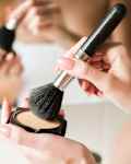 A close-up shot of a woman in a bathroom putting powder on a make-up brush.