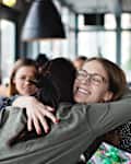 Smiling female friends embracing while holding birthday present sitting at restaurant