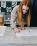 Woman signing documents on a marble kitchen counter, with two people observing.