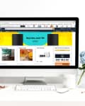 Desktop computer displaying Amazon homepage, on a white desk with a vase of blue flowers, notebooks, and stationery.