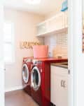 Laundry room with red washer and dryer, white cabinets, abstract wall art, and a patterned laundry basket.