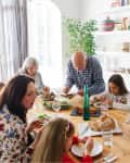Family gathered around a wooden dining table, sharing a meal with salad, bread, and wine, surrounded by bookshelves.
