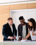 Three people reviewing documents at a kitchen counter, one signing.