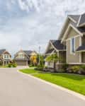 Suburban neighborhood with modern houses, manicured lawns, and a clear sky.