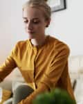 Woman in mustard blouse pouring white wine into a glass on a beige sofa.