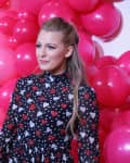 Woman in heart-patterned dress standing in front of pink and gold balloons.