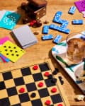 Board game setup with checkers, playing cards, dominoes, popcorn, gummy candies, and drinks on a wooden table.