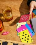 Hands of someone playing cards at table. The cards are bright and colorful. Snacks and other games on table