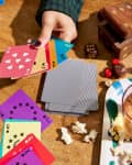 Hands of someone playing cards at table. The cards are bright and colorful. Snacks and other games on table