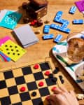 Board game setup with checkers, colorful cards, dominoes, popcorn, drinks, and candy on a wooden table.