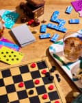 Board game setup with checkers, playing cards, dominoes, popcorn, and drinks on a wooden table.