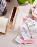 Calculator and receipts on a desk with a gold envelope, pens, and notepads.