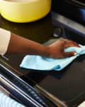 Someone cleaning a black glass stovetop with a blue microcloth
