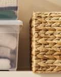 Sweaters folded and stored in plastic storage bin on shelf next to straw storage basket