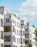 Modern white apartment buildings with balconies and greenery.