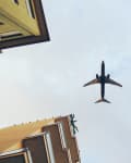 Airplane flying overhead with building corners visible in the foreground.
