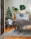 Dining room with Christmas tree, decorated mantel, and table set for a festive meal, viewed through open French doors.