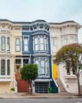 Row of colorful Victorian houses with bay windows and ornate details, featuring black, cream, and blue facades.