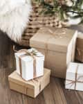 Gift boxes wrapped in brown and white paper with twine bows under a decorated Christmas tree.