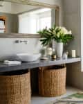 Bathroom with a large mirror, vessel sink, wicker baskets, and a vase of white flowers on the counter.