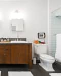 Modern bathroom with double sink vanity, wooden cabinets, white bathtub, and glass shower.