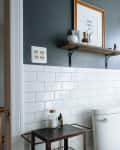 Bathroom with white subway tiles, pedestal sink, wall shelf, and a towel on a ring holder by the window.