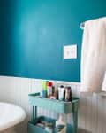 Bathroom with teal walls, white wainscoting, a freestanding tub, and a teal cart holding toiletries.