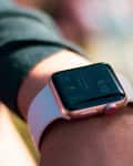 Smartwatch with a pink band displaying 6:13 on a person's wrist.