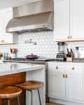 A white kitchen with cookware stored on the stove and the kitchen island