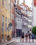 Beautiful bright cityscape in perspective. View on cobbled street with bicycles. Narrow street with colorful buildings in old historic center of Copenhagen. Red tiled roofs. Four people men go forward