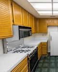 Old 1980s condo kitchen with oak cabinets, tile countertops, gas stove and green flooring.