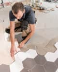 Male worker installing new wooden laminate flooring. The combination of wood panels of laminate and ceramic tiles in the form of honeycomb. Kitchen renovation
