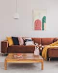 Flowers in vase on wooden coffee table in fashionable living room interior with brown corner sofa with pillows and abstract painting on the wall