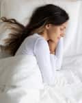 Top above view single serene young woman wearing white sleepwear sleeping lying on one side of bed in the bedroom on comfortable pillow orthopaedic mattress.