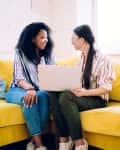 Two friends sitting on sofa with laptop