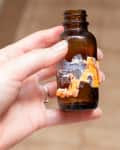 Hand holding small brown bottle/jar with label coming off, sticky, hard-to-remove