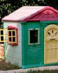 Garden playground for children with lovely little house. Summer kids house in green garden, playhouse cottage for children's play. Green playhouse in a garden.