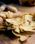 Three russet potatoes peeled and ready for cooking, with leftover peels on the table by the window